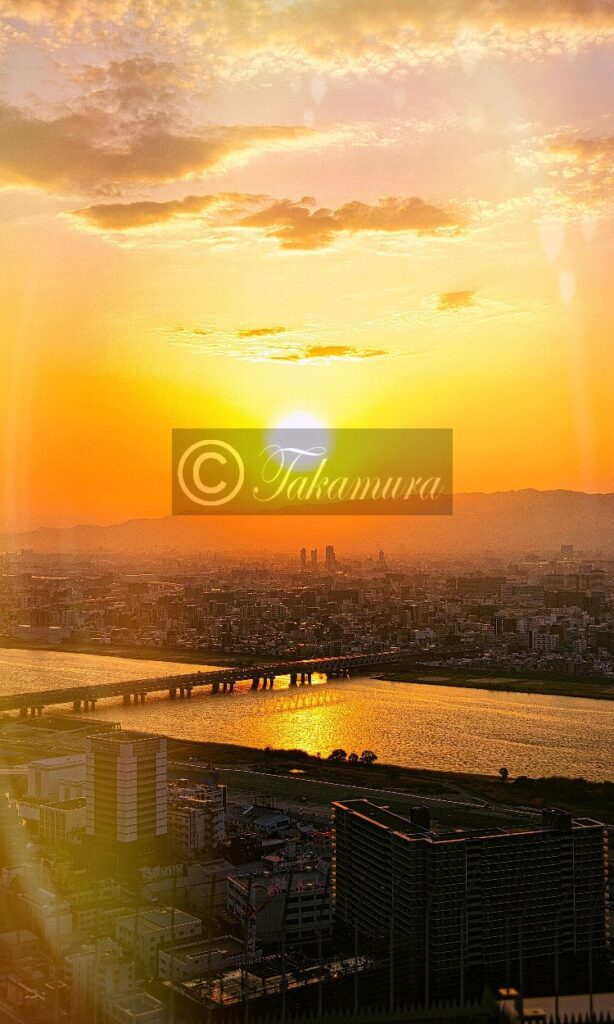 梅田スカイビル展望台から黄色やオレンジ色で沈む太陽のもと淀川や橋、山など夕焼けの写真